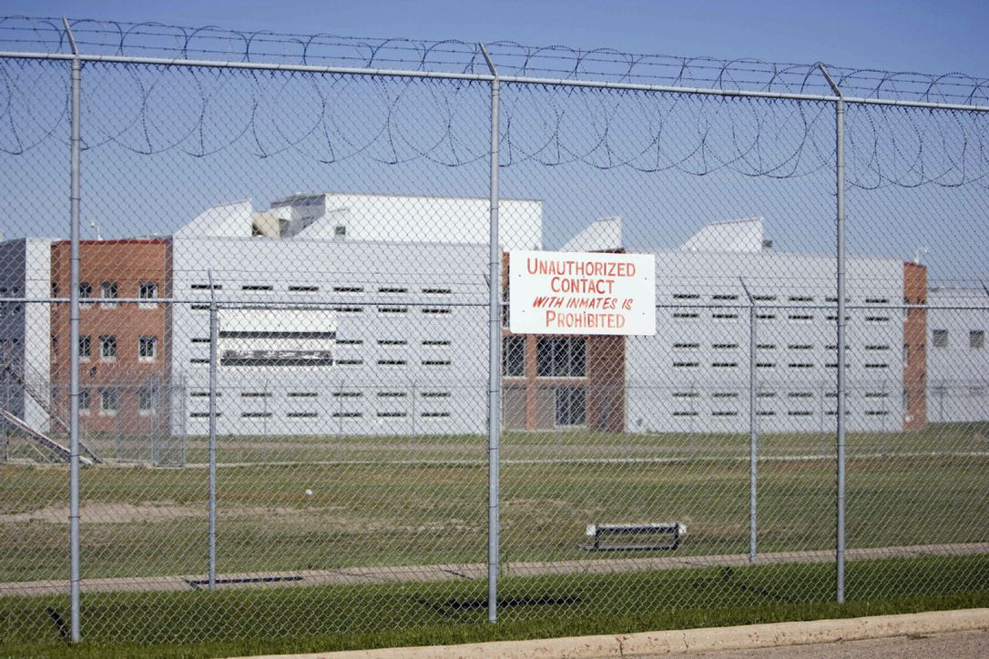 The Regina Provincial Correctional Centre behind a barbed wire fence with a sign on it saying “Unauthorized contact with inmates is prohibited”